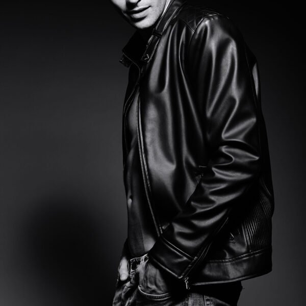 Young handsome muscled fit male model man in leather jacket posing in studio showing his abdominal muscles